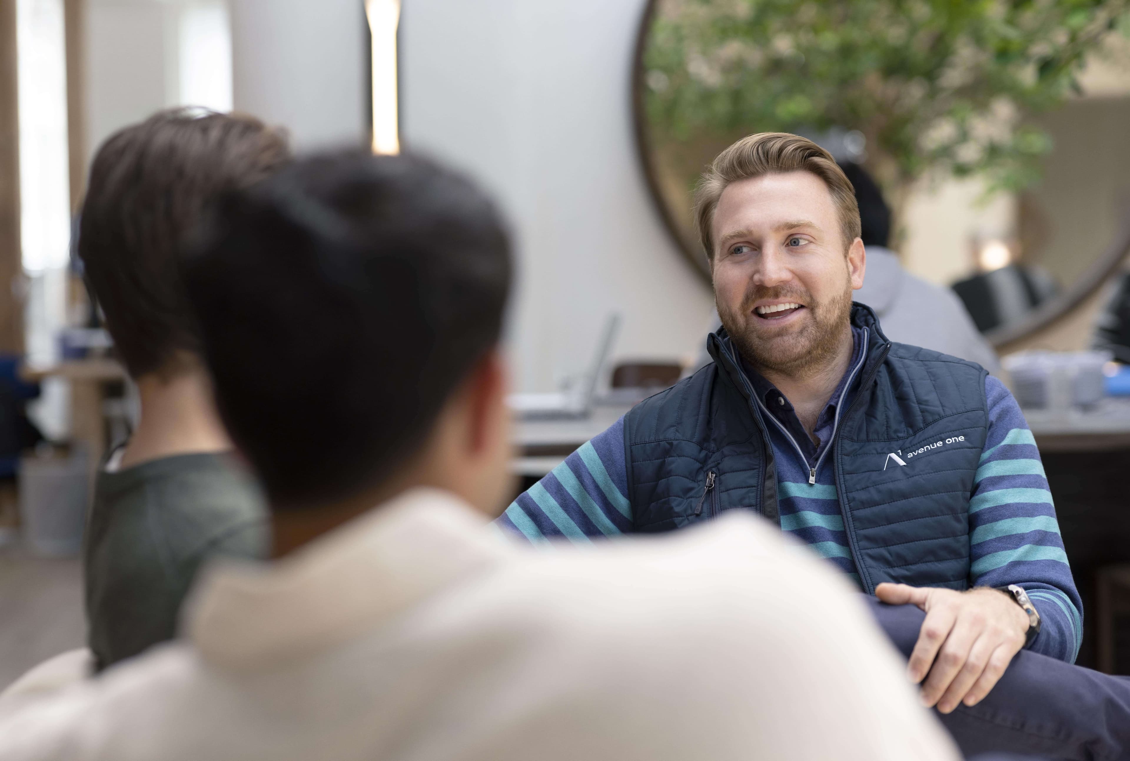 picture of a man sitting on a couch in an office talking to two other people who are not facing the camera